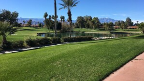 Ein Golfplatz mit Teich, Palmen und Bergen im Hintergrund.
