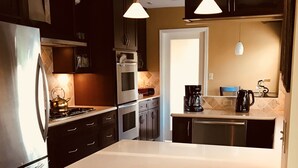 A modern kitchen with dark cabinetry, stainless steel appliances, and pendant lighting. - Charming Floridian Home with pool located close to Lauderdale by the Sea. (Fort Lauderdale)
