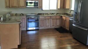 A kitchen with wooden cabinets, a stainless steel oven, a refrigerator, and a window providing natural light. - The Penthouse at Enchanted Acres Ranch (Cocoa)