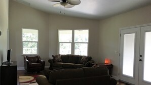 A living room with a ceiling fan, two windows, a door, a television, a couch, a chair, and a rug. - The Penthouse at Enchanted Acres Ranch (Cocoa)