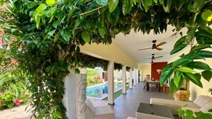 A covered outdoor seating area with a pool in the background.