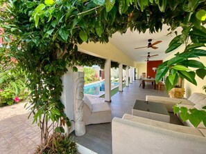 A covered outdoor seating area with a pool in the background.