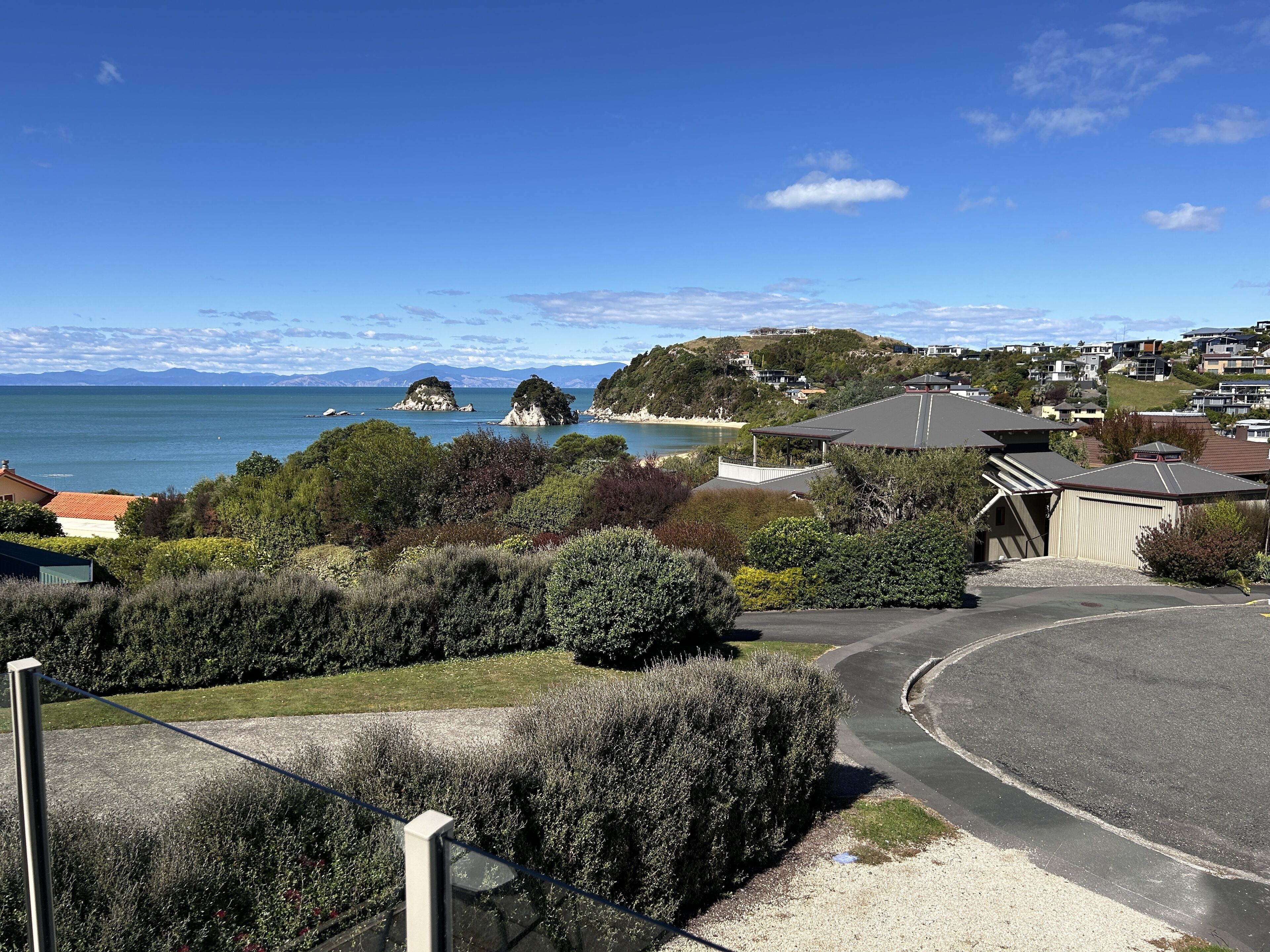 A coastal residential area with houses, a road, and a view of the sea and distant mountains.