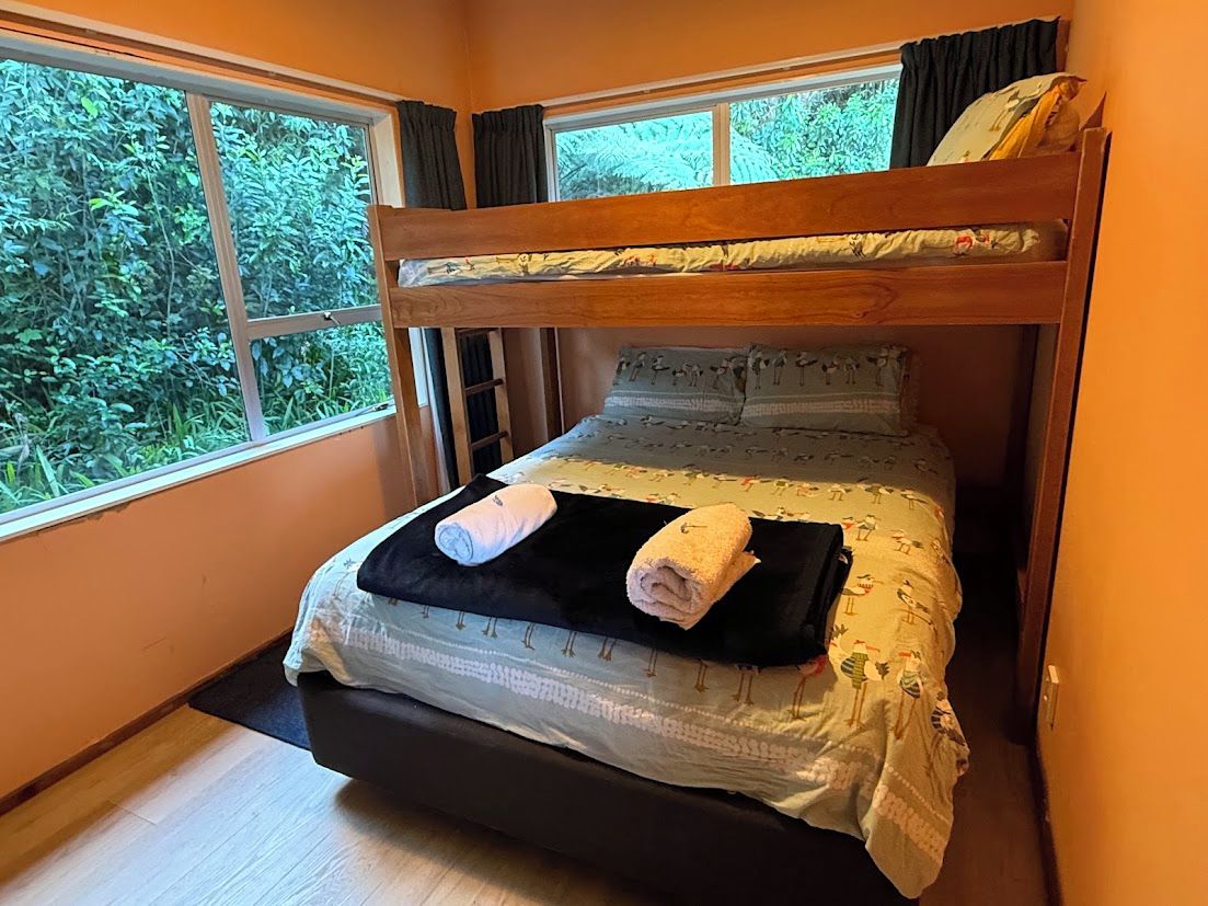 Una cama litera con vista a la vegetación por la ventana, una mesita de noche y una cama con colcha estampada.