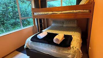Una cama litera con vista a la vegetación por la ventana, una mesita de noche y una cama con colcha estampada.