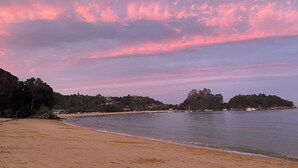 Une plage avec une mer calme, un rivage sablonneux et, en arrière-plan, des arbres et des collines.