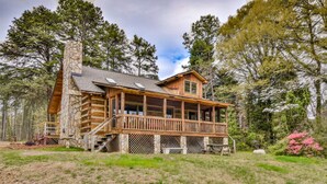 Une cabane en rondins avec une cheminée en pierre, une terrasse en bois et un porche doté de balustrades.