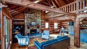 L’intérieur d’un chalet rustique, avec une cheminée en pierre, des poutres en bois, un coin repas et un espace salon confortable.