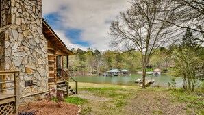 Un bâtiment en pierre doté d’une terrasse en bois et d’un escalier menant à une zone abritée, d’où l’on a vue sur un lac avec des bateaux et des quais.