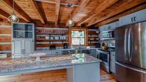 Une cuisine moderne dotée de plans de travail en granit, d’appareils électroménagers en acier inoxydable et de poutres en bois.