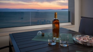 A table with a bottle, two glasses, and a bowl of snacks on a balcony with a view of the ocean at sunset. - Villa Four Brothers - Exclusive Apartment (Podstrana)