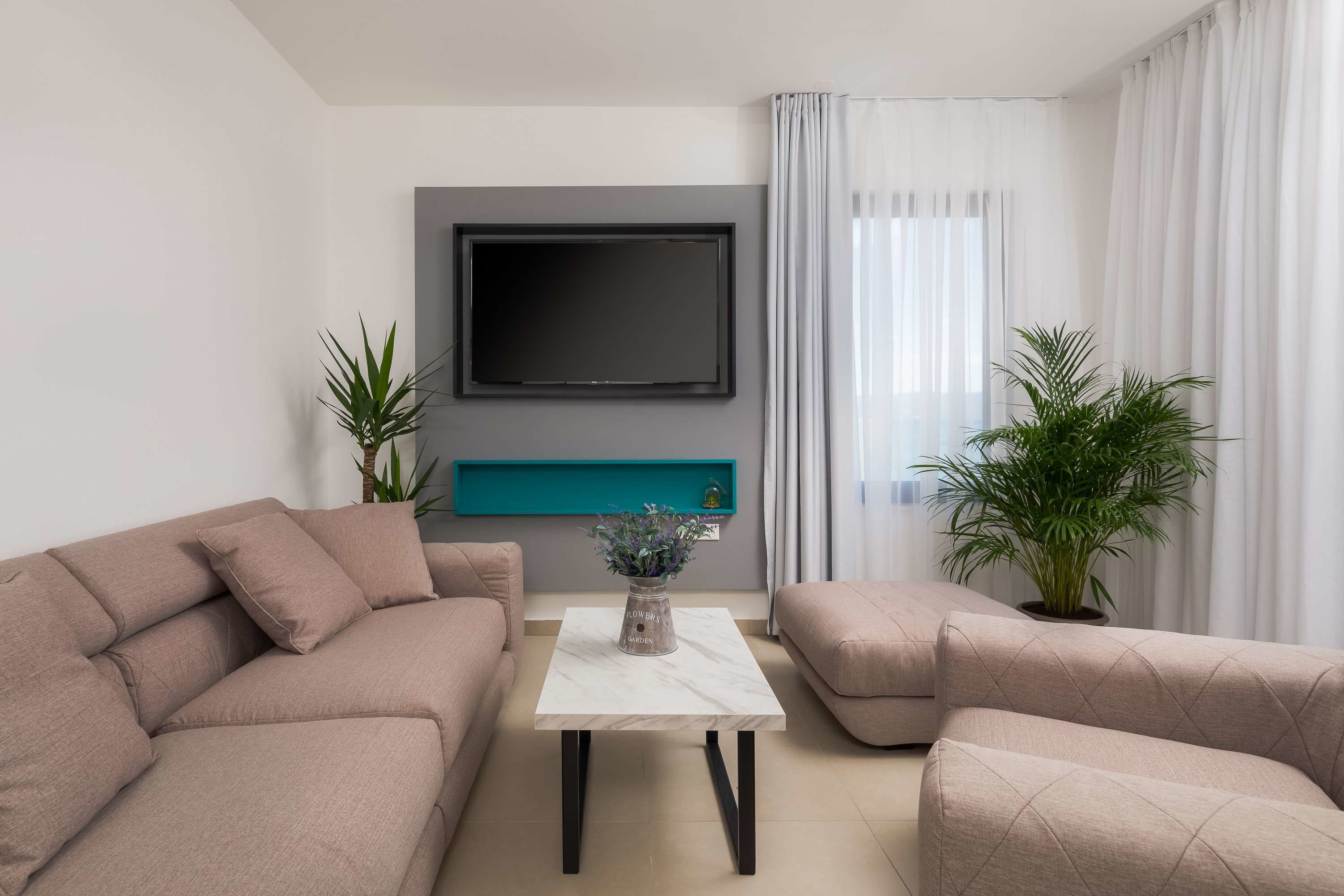 Ein modernes Wohnzimmer mit einer Sofagarnitur, einem Couchtisch, einem wandmontierten Flachbildfernseher und einer Topfpflanze.
