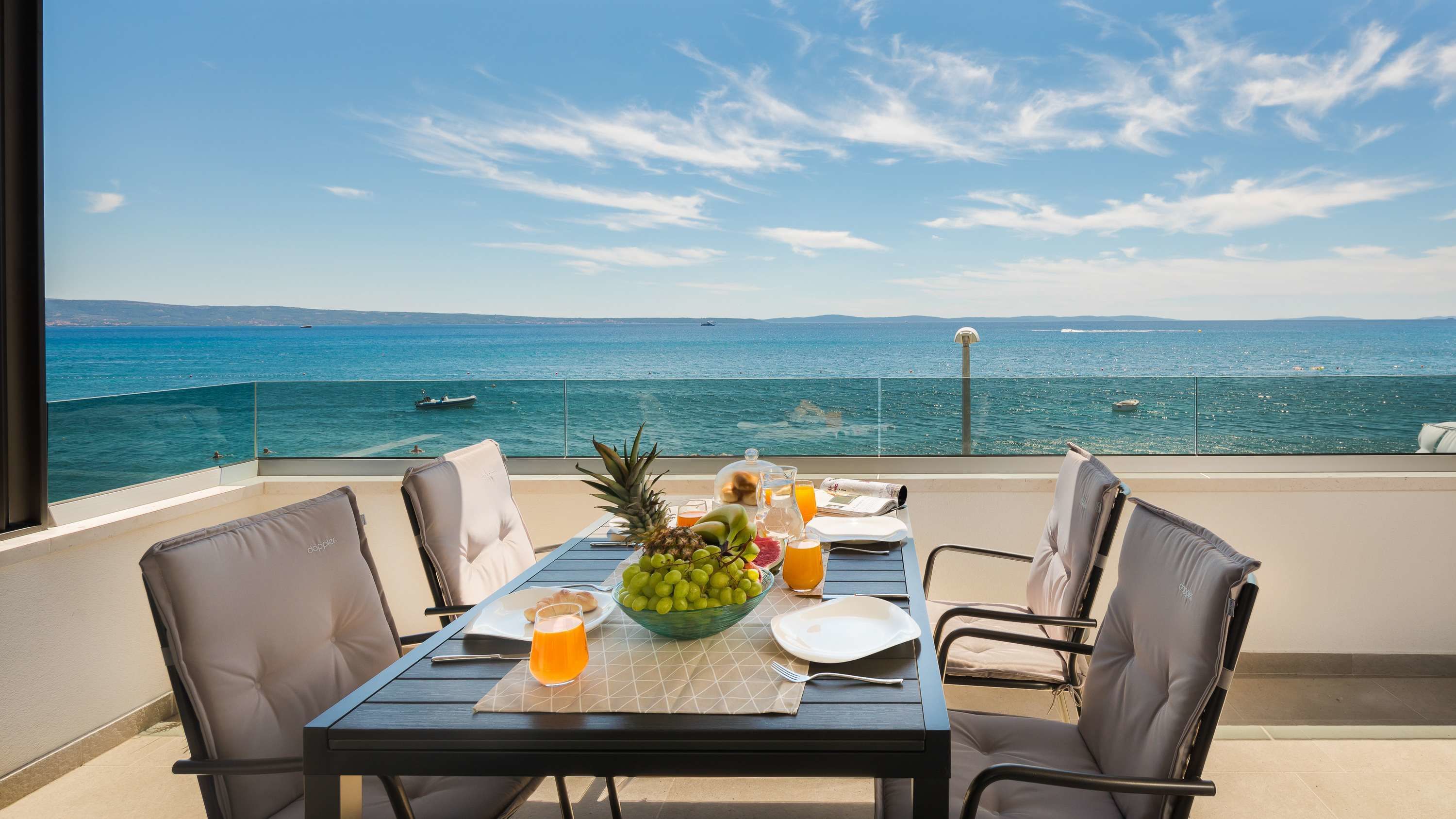A balcony with a table set for breakfast, overlooking the sea.