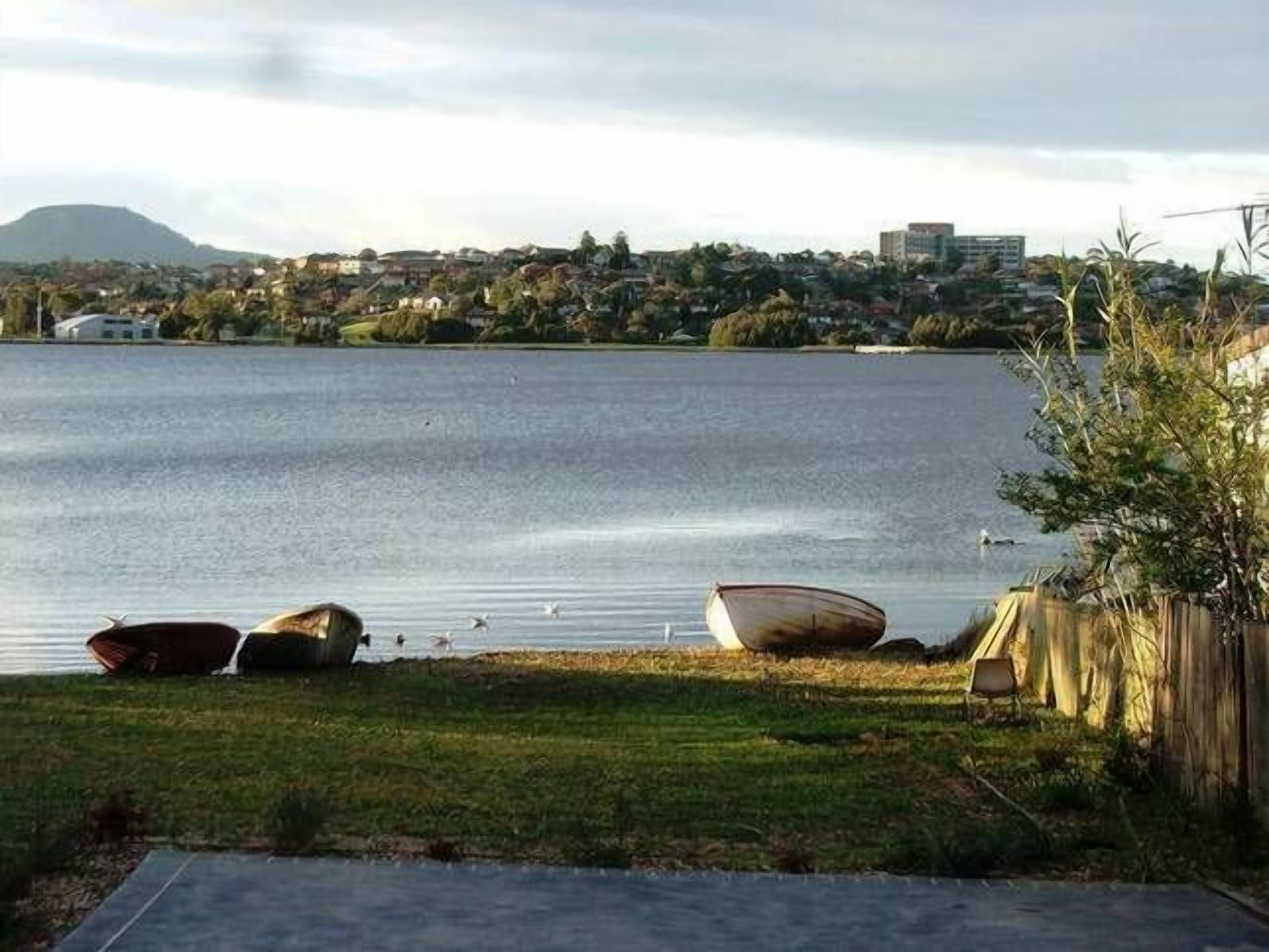 A calm lake with boats on the shore, a grassy area, and a distant cityscape.