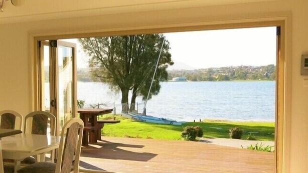 Quarto com porta de vidro deslizante que dá para um deck com vista para um lago e um barco.