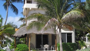 A two-story building with a thatched roof, surrounded by palm trees and a sandy beach.