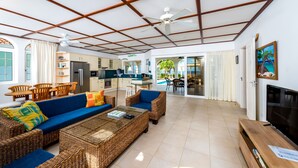 A spacious living area with a blue sofa, wicker furniture, a TV, and a ceiling fan.