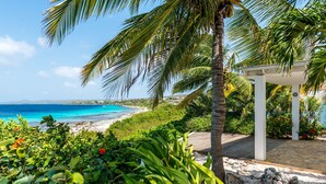 A beach view with a white gazebo, palm trees, and a clear blue ocean.