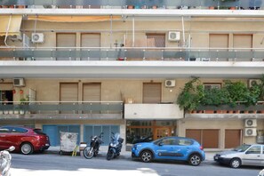 Un immeuble à plusieurs étages doté de balcons, de climatiseurs et où sont stationnés des véhicules.