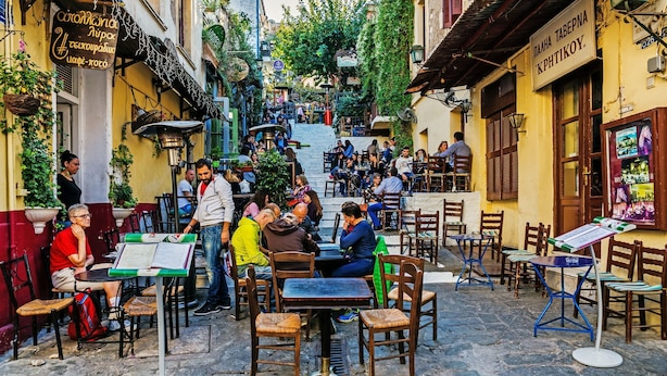 A narrow street with outdoor seating areas, tables, and chairs.
