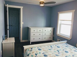Un dormitorio con cama, cómoda, ventilador de techo, puerta y ventana.