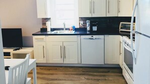 A compact kitchen with white cabinets, a dishwasher, a coffee maker, and a built-in oven.