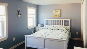 A bedroom with a white bed, a ceiling fan, a window, and a wall decoration.