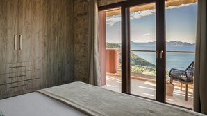 Un dormitorio con un amplio armario de madera, una cama y un ventanal corredero que da a un balcón con vistas al mar y a las montañas.