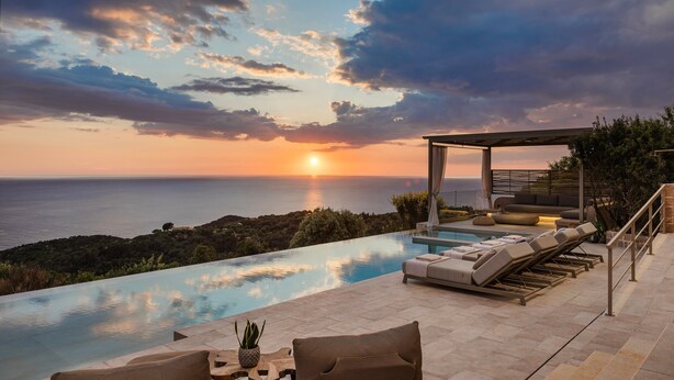 Un área de piscina exterior lujosa con vista al atardecer, zona de estar cubierta y diseño arquitectónico moderno.