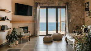 Una sala de estar con pared de piedra, televisor montado, sofá, sillón y vista al mar a través de amplios ventanales.