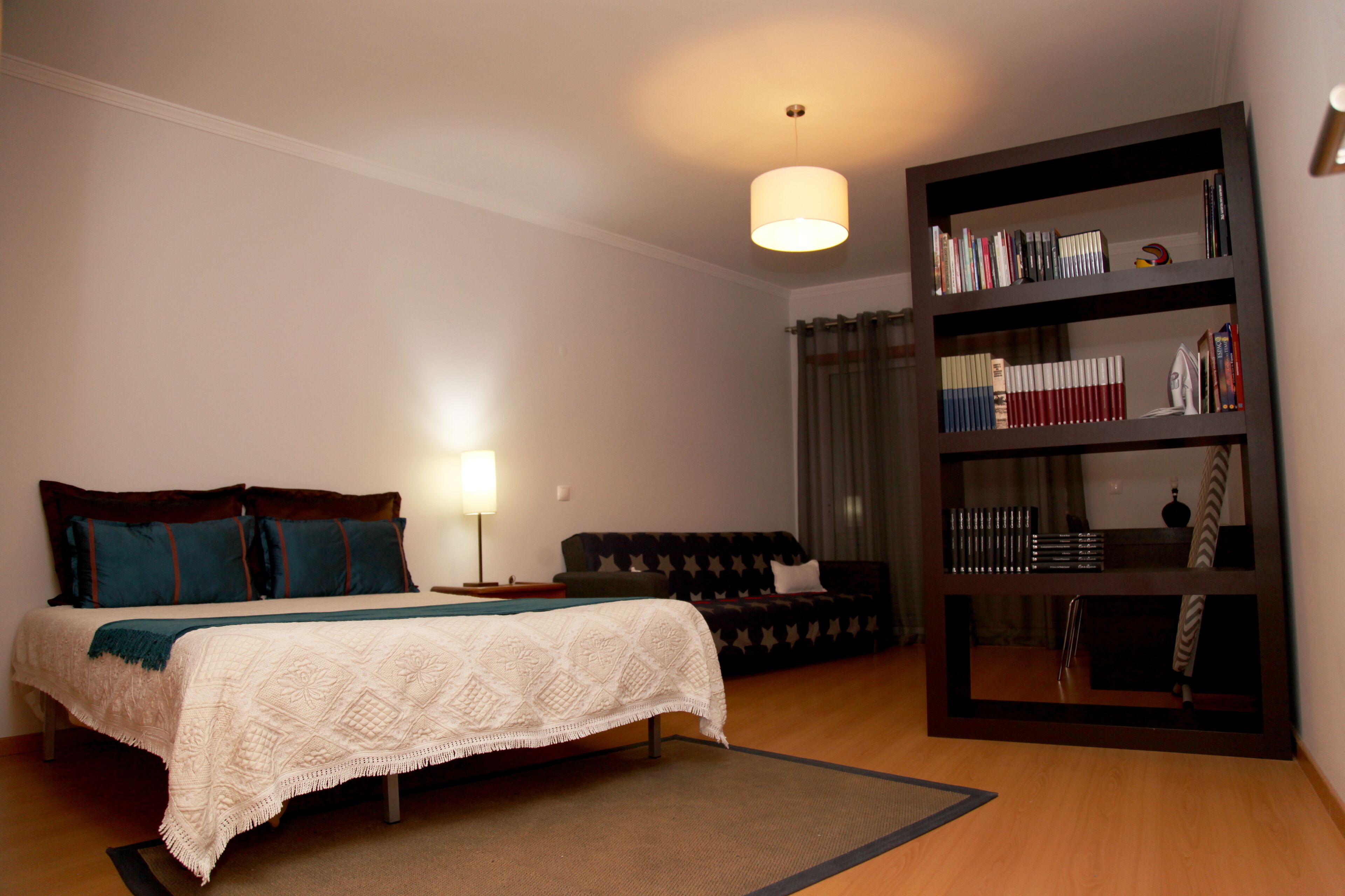 A bedroom with a bed, a nightstand, a bookshelf, and a sofa.