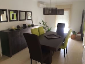 Un comedor con una mesa de madera oscura, sillas verdes y negras, y una lámpara colgante moderna.