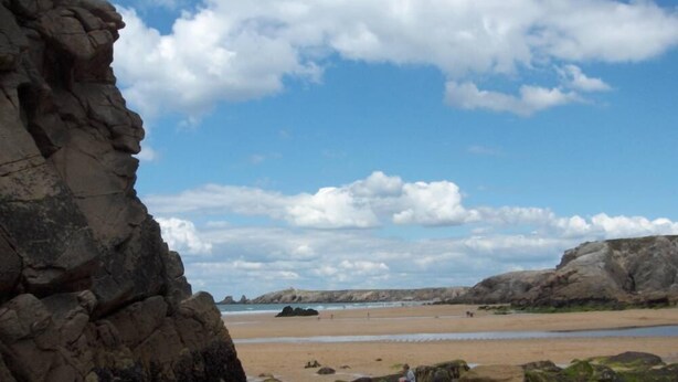 Een kuststrand met grote rotsen en een heldere lucht.