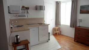 Een compacte keuken met een spoelbak, twee kastjes, een koffiezetapparaat en een klein krukje.