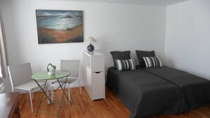 Een kleine, netjes ingerichte kamer met een bed, een stoel, een tafeltje en een bureau.