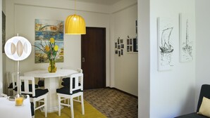 Spiseområde med et hvidt bord, stole, en gul lysekrone og en vase med blomster.