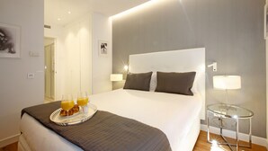 A neatly made bed with a tray of orange juice and croissants, a bedside table with a lamp, and a framed picture on the wall. - Gran Via Boutique (Madrid)