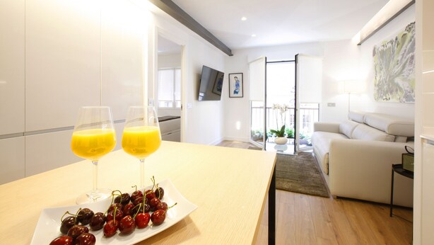 A modern kitchen with a dining area, featuring a table with two glasses of orange juice and a plate of cherries. - Gran Via Boutique (Madrid)
