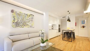 A modern living room with a sofa, a glass coffee table with a white vase, and a kitchen in the background. - Gran Via Boutique (Madrid)