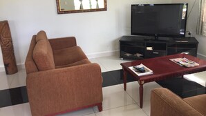 A living room with a brown sofa, a wooden coffee table, a TV on a black stand, and a decorative mirror on the wall. - Malau Lodge (Nuku'alofa)