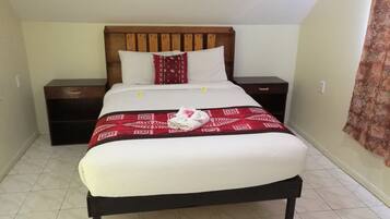 Un lit bien fait, recouvert d’une couvre-lit à motifs rouges, avec des oreillers blancs et une tête de lit en bois. Deux tables de chevet, équipées de tiroirs, sont placées de chaque côté du lit.