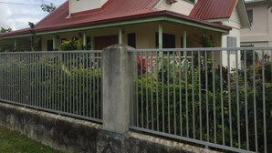 A two-story house with a red roof, green trim, and a grey fence in front. - Malau Lodge (Nuku'alofa)