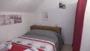 A bedroom with a bed, a wooden headboard, a wall with a picture, and a red curtain. - STUDIO RENTAL DOMAINE DE LA BAUME (CENDRAS)