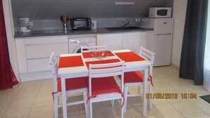 A compact kitchen with a dining table, chairs, a microwave, a toaster, and a washing machine. - STUDIO RENTAL DOMAINE DE LA BAUME (CENDRAS)