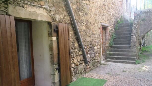 A stone building with a wooden door and a staircase leading to a higher level. - STUDIO RENTAL DOMAINE DE LA BAUME (CENDRAS)