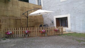 A patio area with a wooden fence, a table with an umbrella, and flower planters. - STUDIO RENTAL DOMAINE DE LA BAUME (CENDRAS)