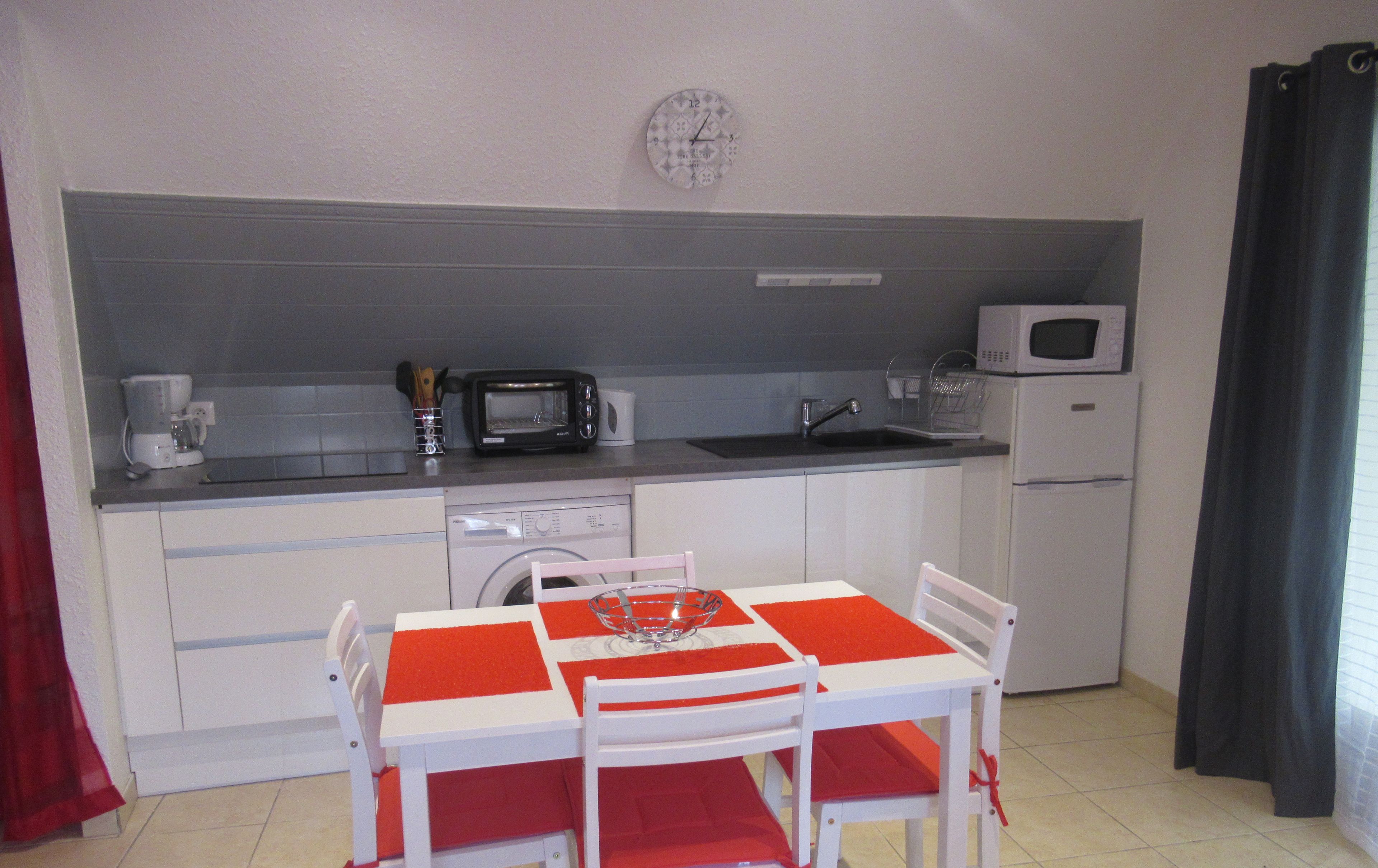 Een kleine keuken met een eettafel, stoelen, een magnetron, een broodrooster en een wasmachine.