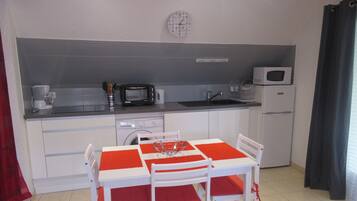 Een kleine keuken met een eettafel, stoelen, een magnetron, een broodrooster en een wasmachine.