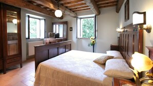 A bedroom with a large bed, wooden ceiling beams, a dresser, a vanity with a mirror, and a window with a view of greenery. - country holiday home - Serrungarina (Serrungarina)