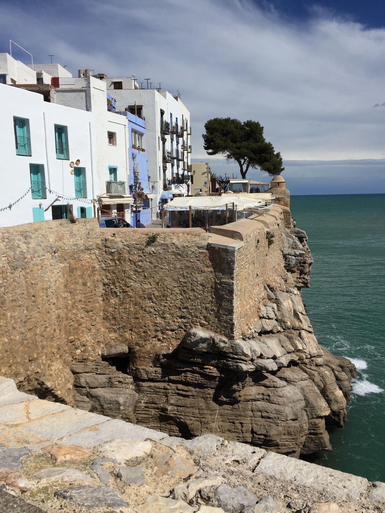 Un edificio costiero con facciata in pietra, un albero sul limitare e vista sul mare.